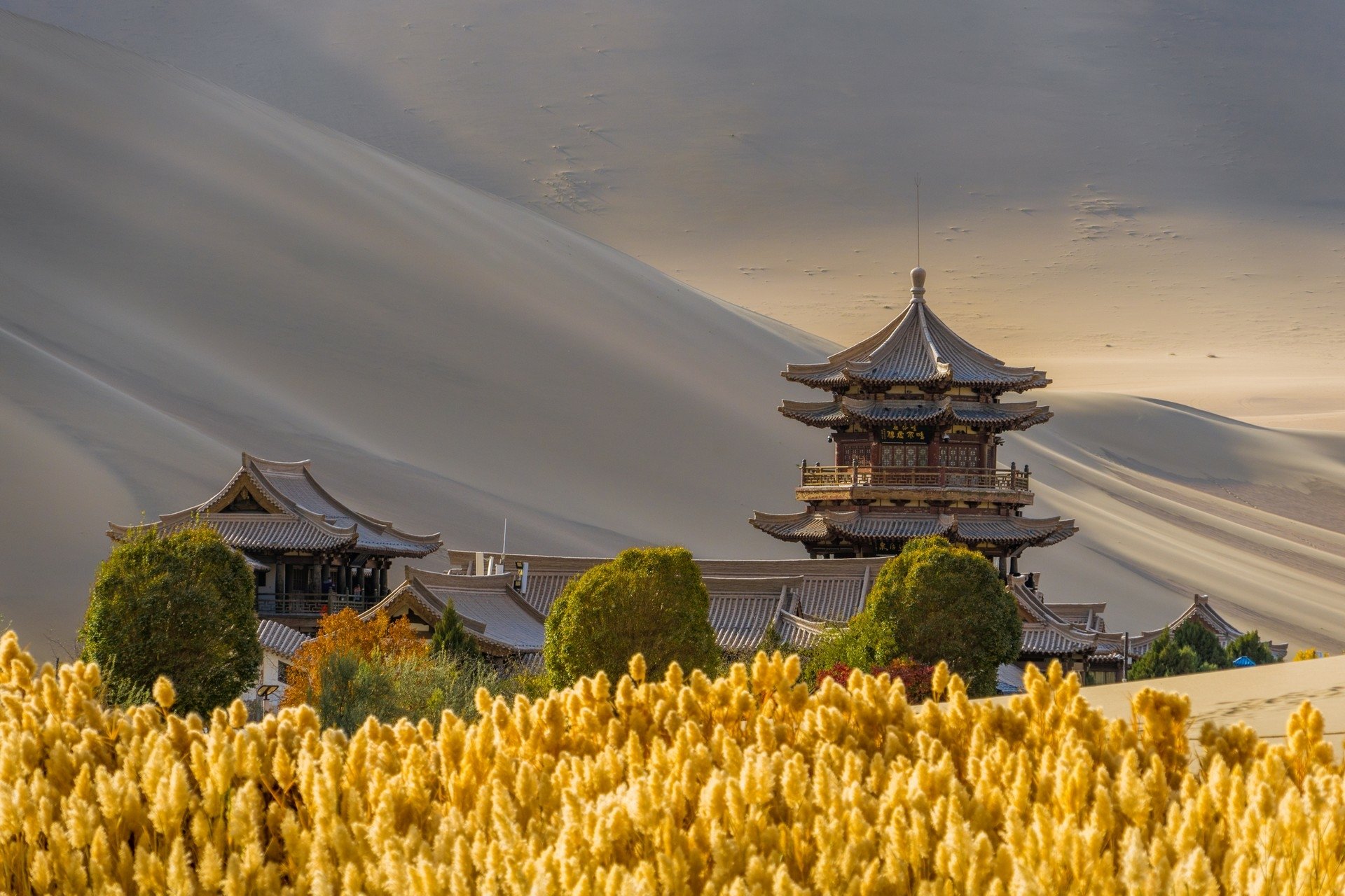 Traditional pavilion and oasis vegetation beneath the Mingsha sand dunes at Dunhuang