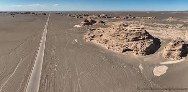 A straight desert road beside weathered rock formations